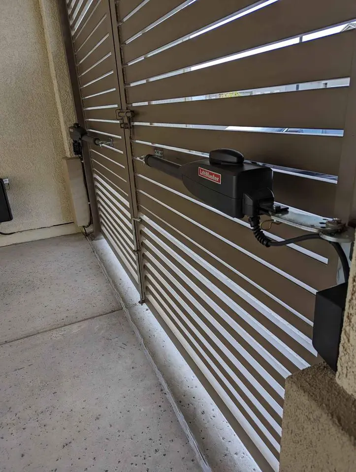 A long, beige vinyl fence crafted by Reno Fence and Gate separates a grassy area from a dirt pathway. Construction tools and materials are scattered along the path. Houses and a clear blue sky are visible in the background, reflecting the quality installation of this sturdy barrier.