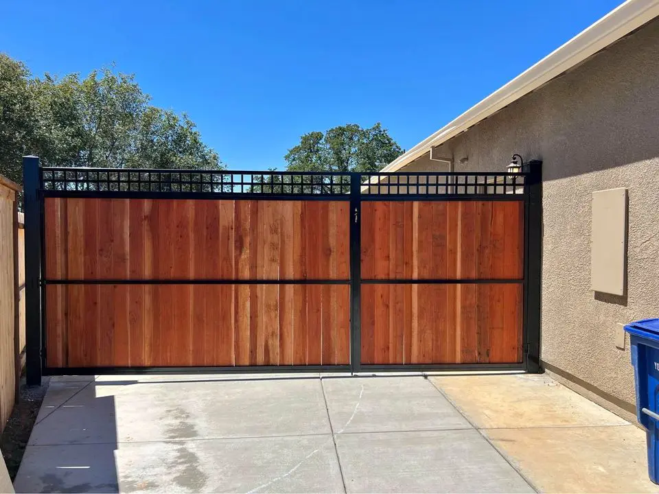 A long white vinyl fence, expertly installed by Reno Fence and Gate, boasts decorative lattice tops running alongside a raised stone-bordered garden. Red flowers bloom in the foreground, with lush green trees visible in the background under a partly cloudy sky.